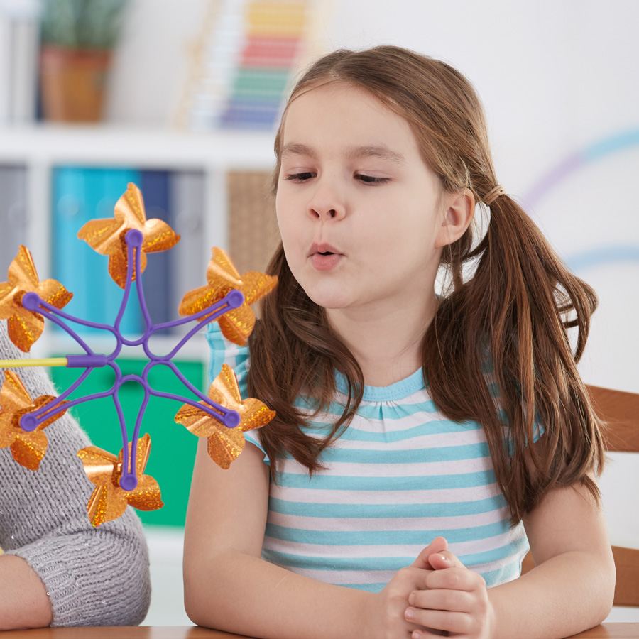 A young girl blowing on a pinwheel toy, creating motion.
