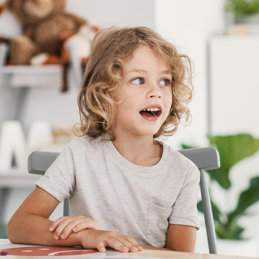 Happy young child sitting at a table, looking excited.
