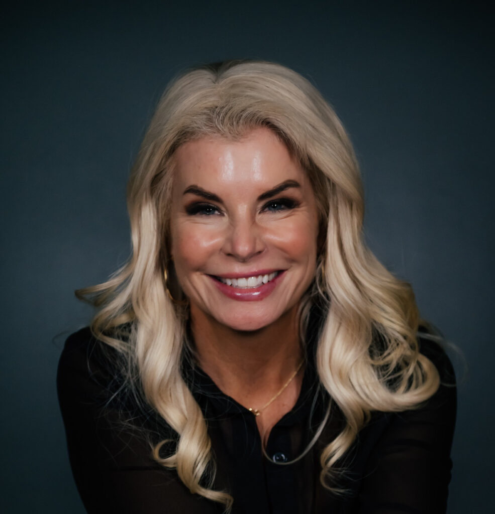 Smiling woman with blonde hair against dark background.