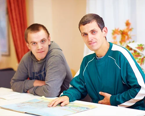 Two young men sitting at a table, smiling and looking at the camera.